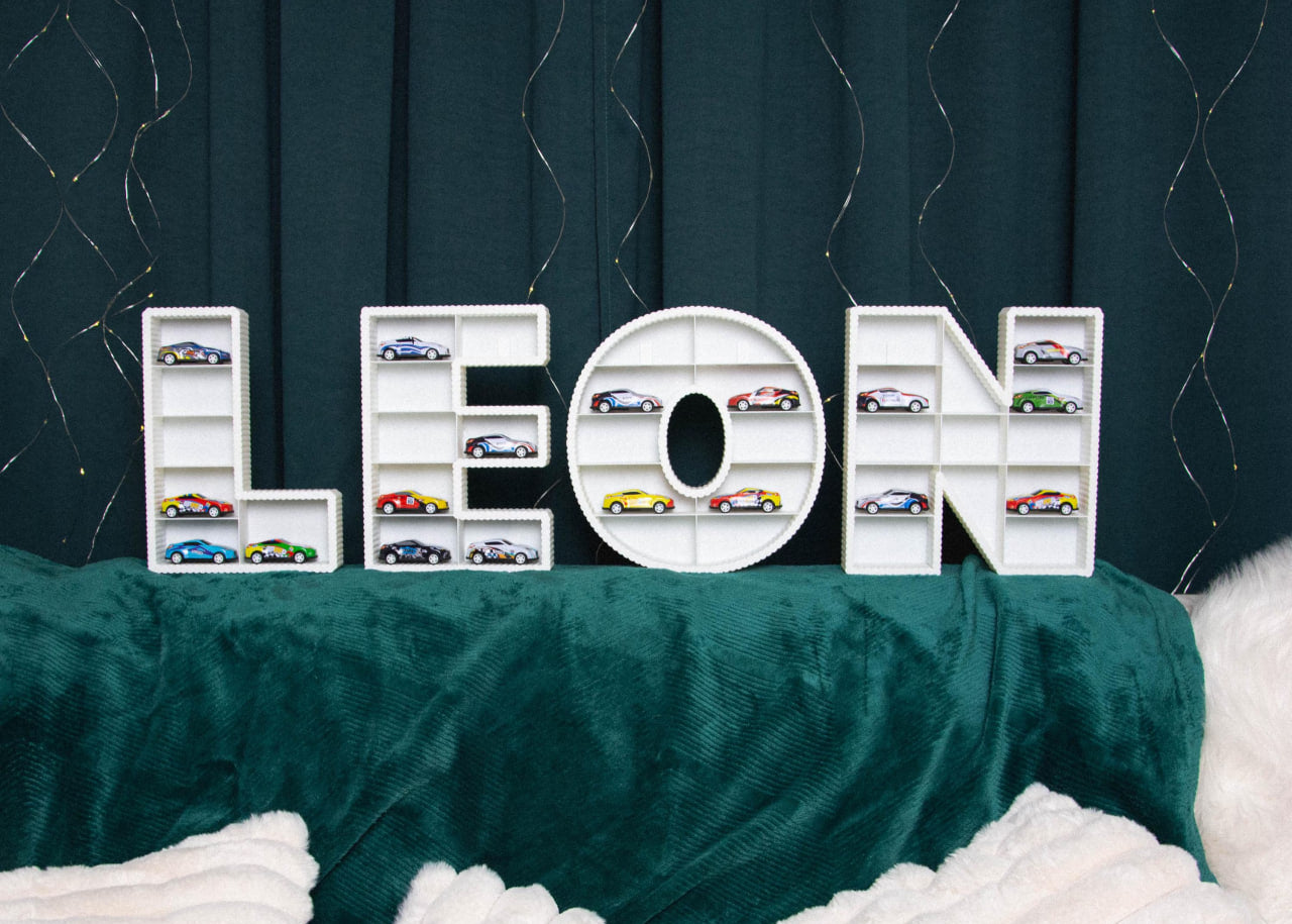 Decorative letters spelling 'LEON' with small car models on a green surface.